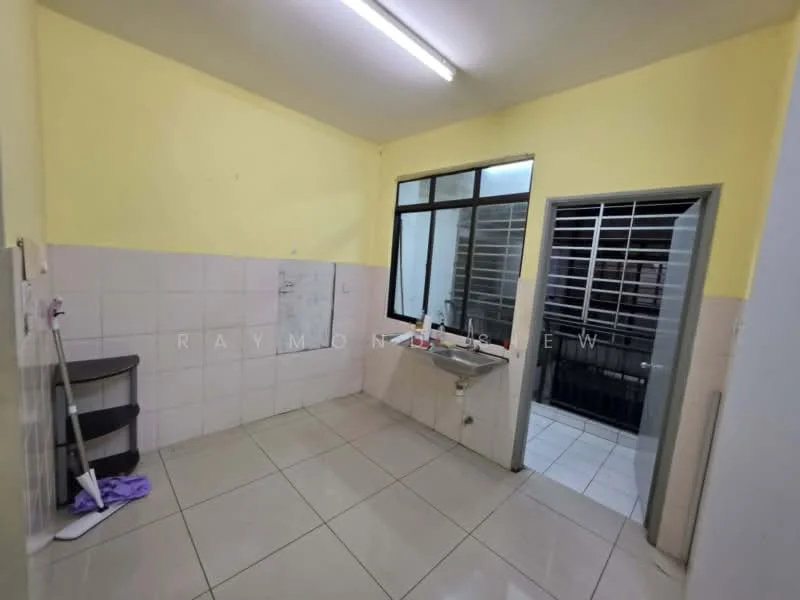 Room features: yellow painted walls, white tiled flooring, single-bowl sink, window with metal grille, door with metal grille, open shelving unit, fluorescent ceiling light, corner space for appliances.