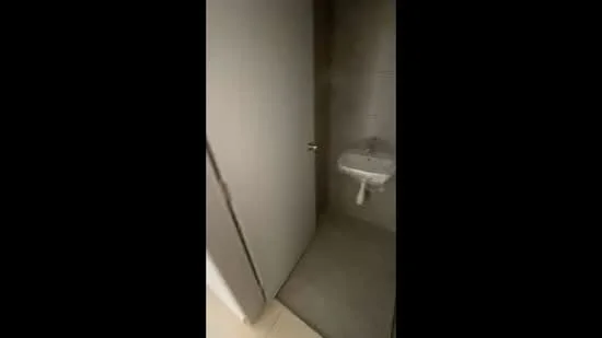 Bathroom features: grey tiled walls, grey tiled flooring, white wall-mounted sink, chrome faucet, white toilet, single mirror above sink, door to bathroom, minimalist design; style: modern.