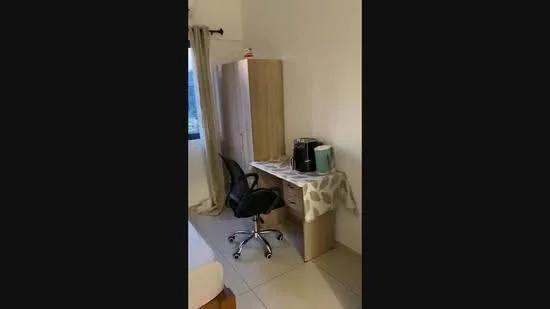 Room features: light-colored walls, tile flooring, window with curtain, wooden wardrobe, desk with chair, coffee machine, small storage drawers, tablecloth.