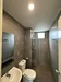 Bathroom features: grey tiled walls, grey tiled flooring, walk-in shower with glass enclosure, rain shower head, handheld shower, single-sink vanity with wall-mounted mirror, one-piece toilet, chrome basin mixer, recessed downlights, window for natural light; style: modern.