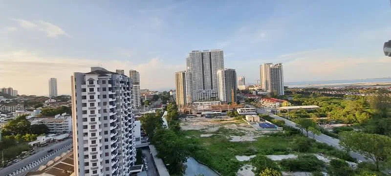 Exterior type: high-rise condominium; features: multiple high-rise buildings, urban skyline, green landscaping, open land area, view of the sea, surrounded by residential buildings, clear blue sky, road access, construction site visible, mature trees; style: modern.