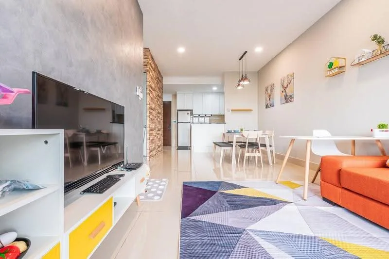 Living features: orange fabric sofa, white coffee table, TV console with storage, wall-mounted TV, area rug with geometric pattern, decorative wall art, open shelving unit, recessed downlights, grey accent wall, cream tiled flooring; style: modern. Kitchen features: white cabinetry, stainless-steel fridge, built-in oven, 4-burner gas hob, white countertop, open-plan layout; style: modern.