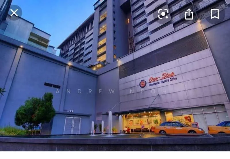 Exterior type: mixed-use building; features: grey painted facade, glass curtain wall, projecting balconies, entrance with awning, landscaped area with plants, taxi drop-off area, multiple storeys, illuminated signage; style: modern.