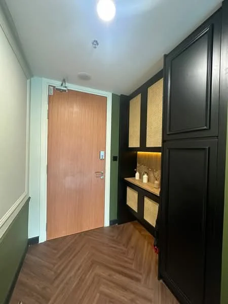 Room features: wooden door with metal handle, black cabinetry with rattan panels, built-in shelf with lighting, laminate flooring in herringbone pattern, green painted walls, ceiling light fixture, wall-mounted light switch; style: modern.