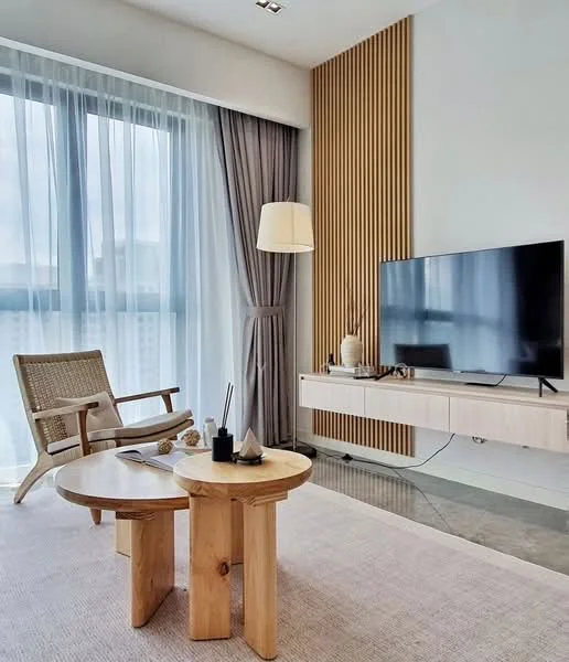 Living features: wooden coffee table with two cylindrical legs, fabric area rug, flat-screen TV on wall-mounted console, woven armchair, floor lamp, curtains with sheer and blackout layers, wood panel accent wall, concrete flooring, decorative items on console; style: modern.