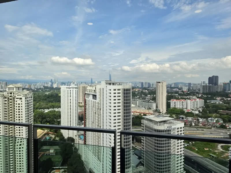 Exterior type: high-rise condominium; features: city skyline view, glass balcony railing, surrounded by greenery, multiple high-rise buildings, urban landscape, clear blue sky with clouds; style: modern.