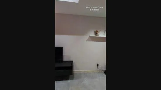 Room features: light grey painted walls, shelf on wall, black TV console, flooring with light grey tiles, electrical outlet on wall.