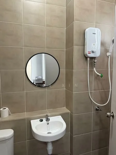 Bathroom features: cream tiled walls, cream tiled flooring, round mirror with black frame, white wall-mounted sink, chrome faucet, toilet roll holder, white one-piece toilet, water heater unit, shower head, green water control knob; style: modern.
