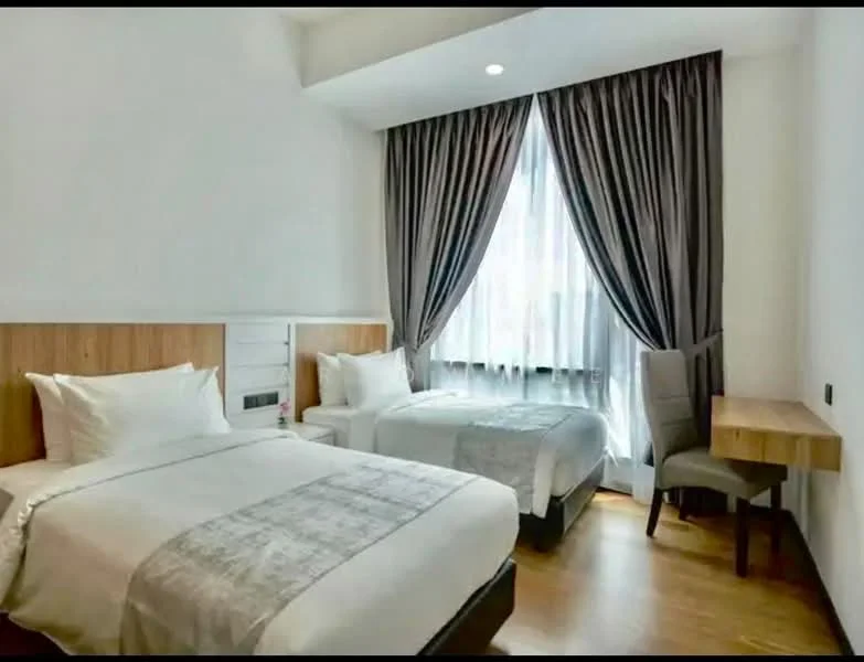 Bedroom features: two single beds with white bedding, wooden headboards, wooden bedside table, grey upholstered chair, window with sheer curtains, dark grey curtains, wooden flooring, recessed ceiling lights; style: modern.