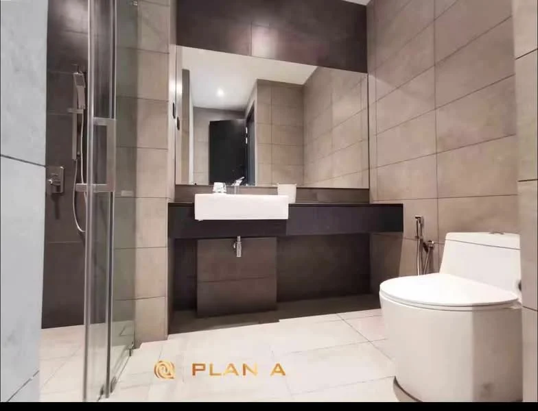 Bathroom features: grey tiled walls, light grey floor tiles, single-sink vanity with dark cabinetry, white rectangular sink, chrome basin mixer faucet, framed mirror above vanity, walk-in shower with glass enclosure, chrome shower head, one-piece toilet, toilet paper holder, built-in shelving, recessed lighting; style: modern.