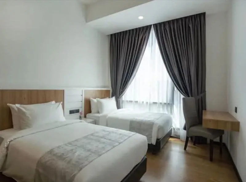 Bedroom features: two single beds with white bedding, wooden headboards, wooden bedside table, grey upholstered chair, desk with wooden surface, floor-to-ceiling window, sheer curtains, dark grey curtains, wooden flooring, recessed downlights; style: modern.