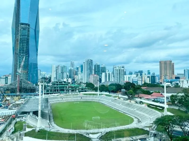 Exterior type: high-rise condominium; features: city skyline view, surrounded by urban landscape, visible sports stadium, construction site in foreground, green field, multiple high-rise buildings, cloudy sky; style: modern.