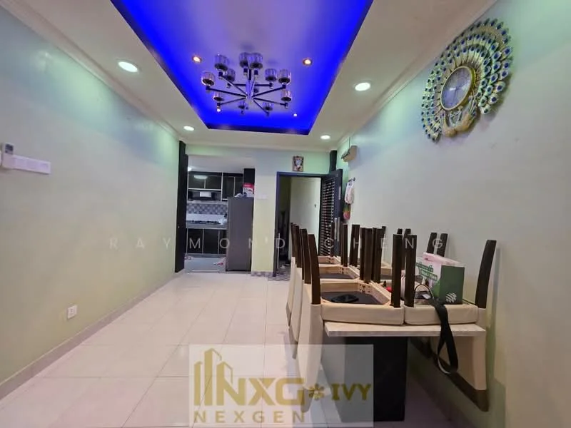 Room features: white painted walls, recessed ceiling with blue LED lighting, tile flooring, chandelier with multiple bulbs, wooden dining chairs stacked, open layout, kitchen area visible in the background, wall-mounted clock, decorative wall art; style: modern.