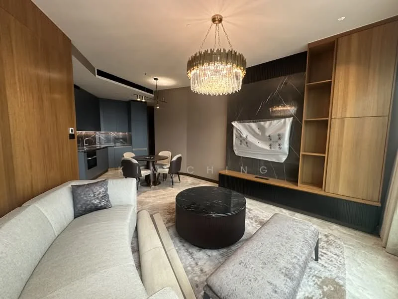 Living features: curved grey fabric sofa, round black marble coffee table, light grey upholstered bench, chandelier with crystal accents, wood panel feature wall, built-in shelving unit, marble accent wall, recessed lighting, dining table with four chairs, kitchenette with grey cabinetry, floor-to-ceiling windows with sheer curtains, neutral-toned area rug; style: modern.