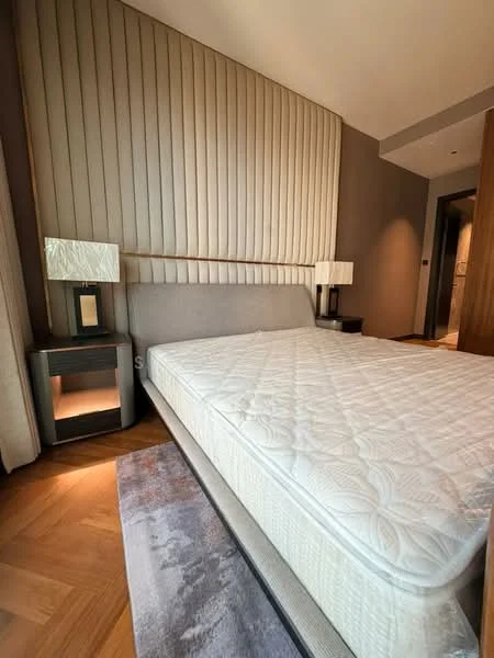 Bedroom features: upholstered headboard, queen-size bed, wooden bedside tables, table lamps with square bases, textured wall paneling, wood flooring, area rug with geometric pattern, neutral color scheme; style: modern.