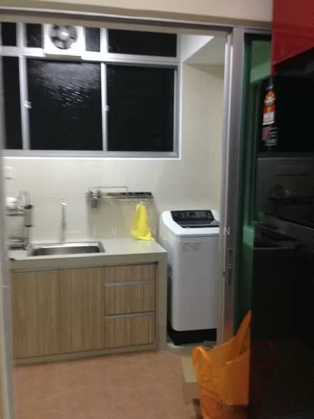 Kitchen features: single-bowl stainless-steel sink, chrome pull-down faucet, wood cabinetry with light brown finish, built-in washing machine, white tiled backsplash, cream-colored walls, tile flooring, large window for natural light, metal wall rack for utensils, orange plastic bag on the floor; style: modern.