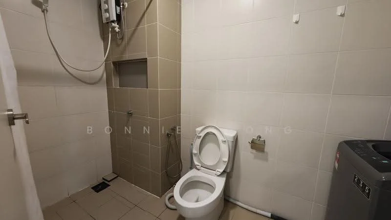 Bathroom features: white ceramic toilet, shower area with wall-mounted shower head, grey tiled walls, light beige tiled flooring, washing machine, water heater, toilet paper holder, wall-mounted soap dish.