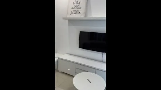 Living features: white painted walls, light-colored flooring, wall-mounted TV, TV console with drawers, round coffee table, decorative wall art, shelves above TV console; style: modern.