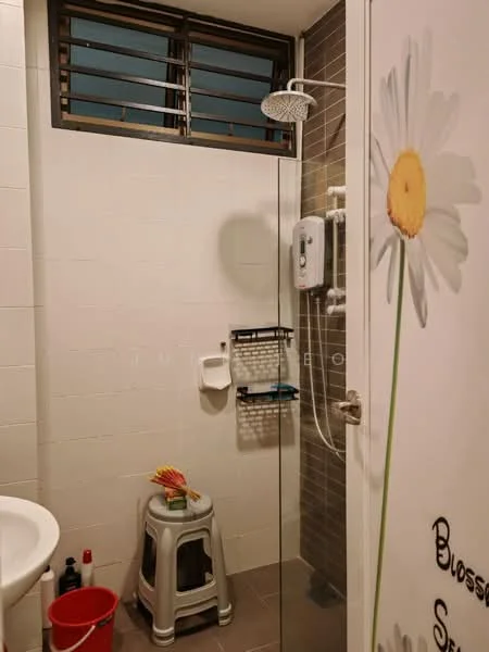 Bathroom features: shower with glass enclosure, rain shower head, wall-mounted shower control, white tiled walls, grey tiled accent wall, ceramic tile flooring, toilet, small stool, wall-mounted storage rack, decorative wall art with flower design, window with metal grille, bucket; style: modern.