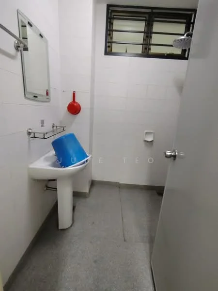 Bathroom features: white tiled walls, grey tiled flooring, sink with pedestal, mirror above sink, shower head, toilet, red wall-mounted hook, blue bucket.