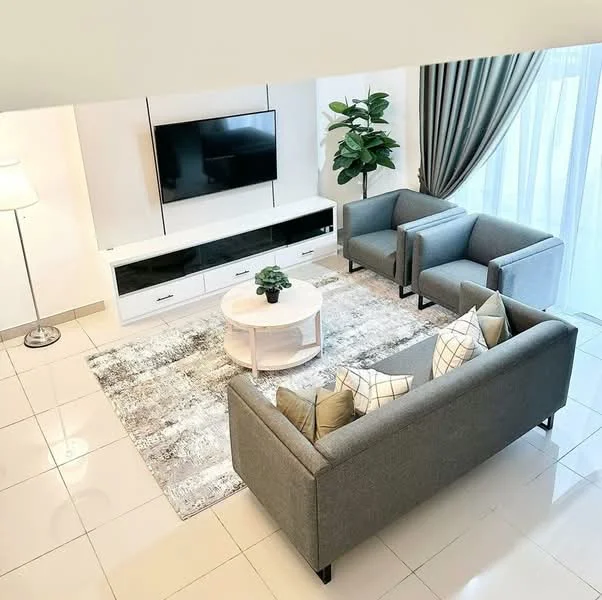 Living features: grey fabric 3-seater sofa, 2 grey armchairs, white circular coffee table, TV console with storage, wall-mounted flat-screen TV, area rug with geometric pattern, floor lamp, potted plant, curtains, large windows with natural light, glossy tiled flooring, decorative cushions; style: modern.
