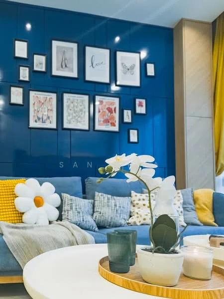Living features: blue accent wall, framed artwork on wall, 3-seater fabric sofa in blue, yellow throw pillows, white daisy-shaped cushion, decorative plant in white pot, wooden coffee table, green glass candle holder, white candle, decorative tray, curtains in yellow fabric; style: modern.