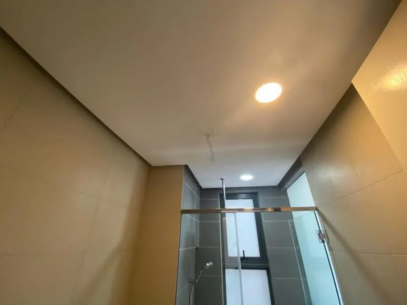 Bathroom features: recessed downlights, glass shower enclosure, tile cladding, neutral painted walls, modern ceiling, shower head, sliding glass door, window for natural light; style: modern.