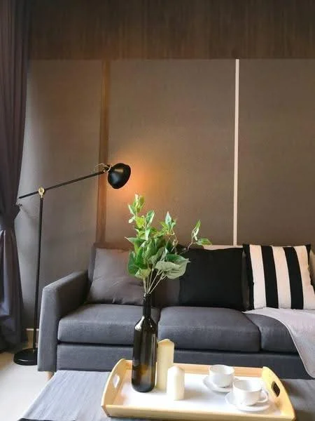 Living features: grey fabric sofa, black and white striped cushions, floor lamp with black shade, wooden coffee table, decorative vase with greenery, white candles, dark accent wall, curtains in dark fabric; style: modern.