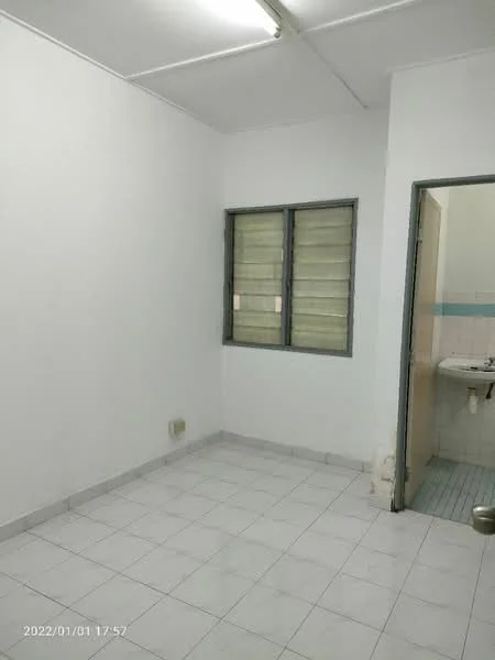 Room features: white painted walls, white tiled flooring, single window with metal grille, flush door, light fixture on ceiling, visible plumbing fixtures in adjacent area.