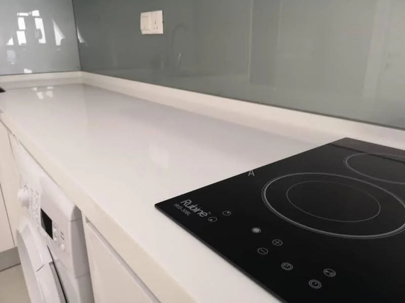 Kitchen features: white countertop, induction cooktop, built-in oven, white cabinetry, grey backsplash, integrated dishwasher, modern faucet, recessed lighting; style: modern.