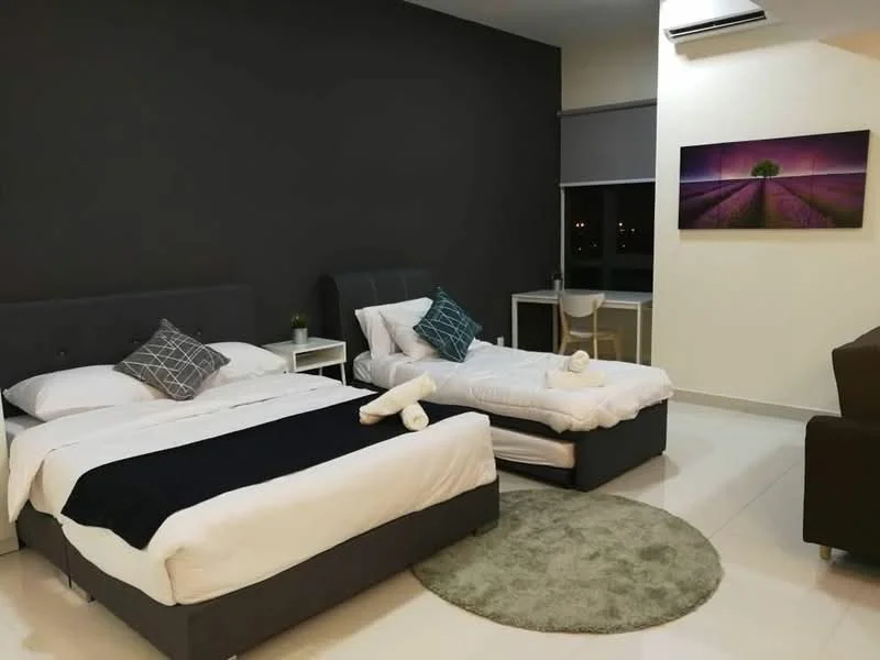 Bedroom features: two beds: one king-size bed and one single bed, grey upholstered bed frames, white bedding with black throw blanket, decorative pillows, nightstand with lamp, study desk with chair, area rug in circular shape, wall-mounted air conditioning unit, large window with roller blinds, framed artwork on wall, cream painted walls, tile flooring; style: modern; view: city.