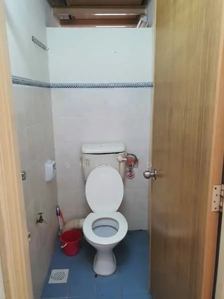 Bathroom features: white toilet, single-sink vanity, blue tile flooring, white tiled walls, mirror above sink, toilet paper holder, red bucket, door with wooden finish, light fixture on ceiling.