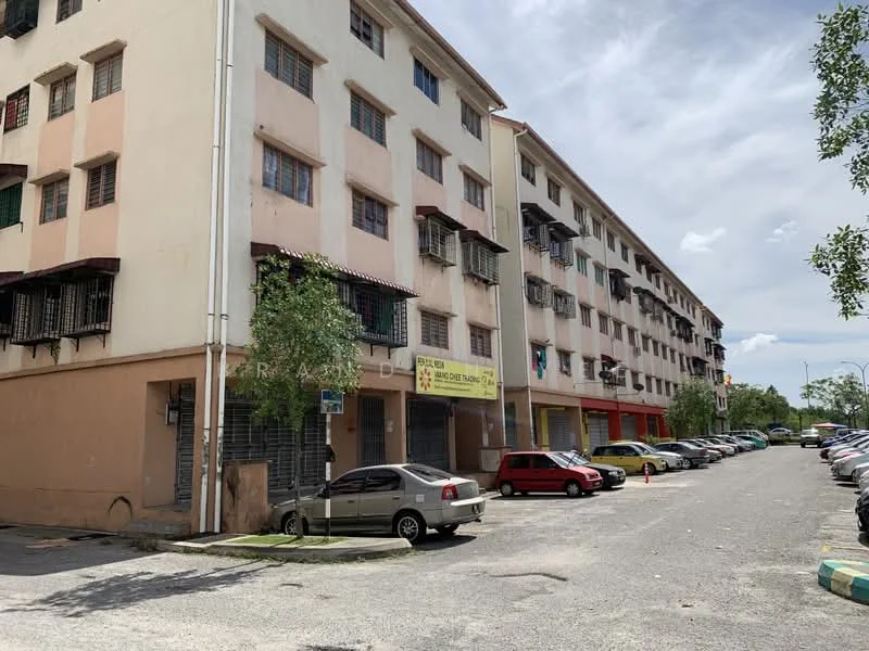 Exterior type: low-rise apartment block; features: cream painted facade, multiple floors, balconies with metal railings, ground-level parking area, visible signage on ground floor, trees and greenery along the building, asphalt parking lot, variety of parked cars; style: modern.