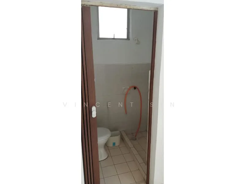 Bathroom features: white toilet, tile flooring, white tiled walls, window for natural light, shower hose, small bucket, door with wooden frame.