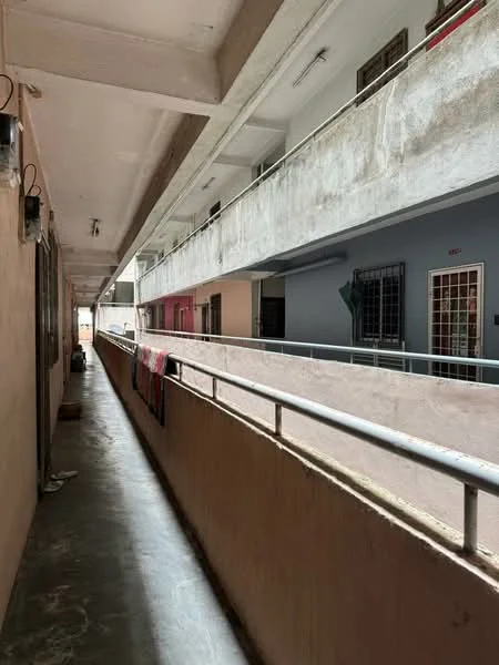 Room features: concrete flooring, exposed concrete ceiling, metal railing, painted walls in beige and grey, window grilles, laundry hanging on railing, light fixtures on ceiling, corridor layout; style: modern.