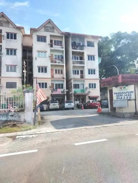 Exterior type: low-rise apartment block; features: 3-storey building, white painted facade, balconies on each floor, visible parking area, landscaped entrance, flagpole with Malaysian flag, signage for 'Pangsapuri Seri Jasa', surrounded by greenery; style: modern.