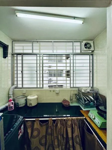 Kitchen features: green countertop, stainless-steel sink, wall-mounted split AC, window with metal grille, curtains with circular pattern, dish rack, rice cooker, stove, kitchen cabinets, washing machine, wall-mounted shelves.