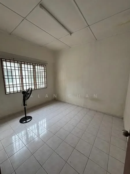 Room features: white painted walls, ceiling with fluorescent lights, tiled flooring, window with metal grille, standing fan, empty space.