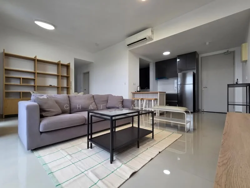 Living features: 3-seater fabric sofa in grey, coffee table, area rug, open shelving unit, wall-mounted air conditioning unit, flat-screen TV, kitchenette with black cabinetry, refrigerator, light-colored walls, polished concrete flooring, ceiling light fixture; style: modern.