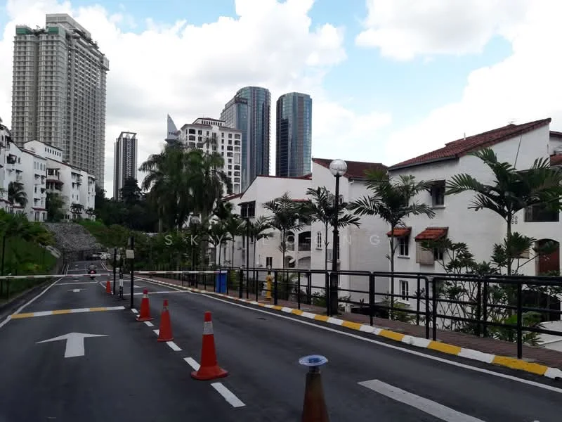 Exterior type: linked terrace house; features: white painted facade, red tiled roof, palm trees, manicured landscaping, guard house at entrance, street with traffic cones, surrounded by high-rise buildings, paved road, lampposts, greenery along the road; style: traditional.