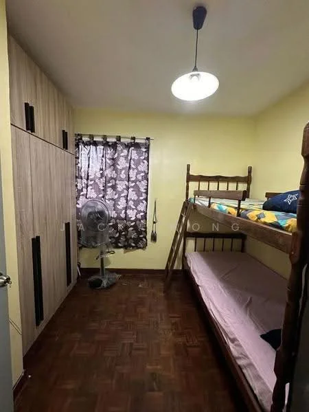 Bedroom features: bunk bed with wooden frame, single mattress on top bunk, single mattress on bottom bunk, wooden wardrobe with sliding doors, brown parquet flooring, yellow painted walls, floral patterned curtains, ceiling light fixture, standing fan.