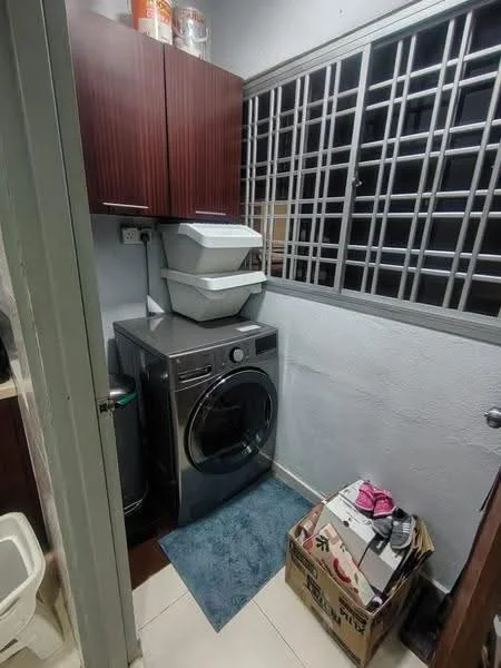 Laundry features: front-load washing machine, wood cabinetry in dark brown, white countertop, grey area rug, tile flooring, window with metal grille, storage bins on top of cabinetry, cardboard box on floor, shoes on floor.