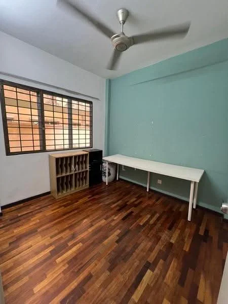 Room features: light brown wooden flooring, green accent wall, white painted walls, ceiling fan, large windows with metal grills, white table, wooden shelving unit, corner space for storage; style: modern.