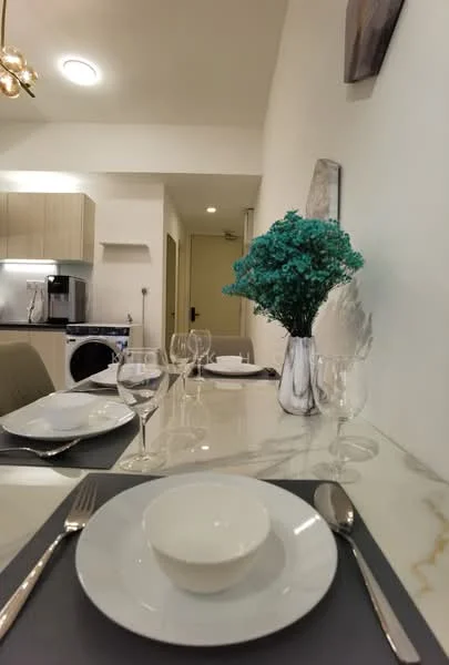 Dining features: marble dining table, white plates, glass wine glasses, cutlery, decorative vase with flowers, grey placemats, modern pendant light, wall-mounted artwork, open kitchen view, washing machine visible in background; style: modern.
