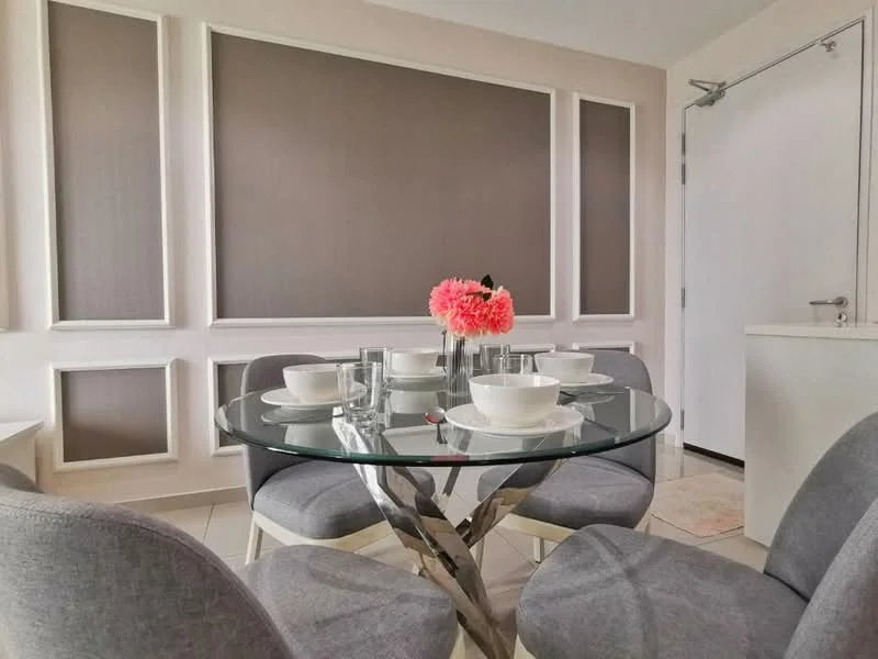 Dining features: round glass dining table, 6 upholstered dining chairs in grey, decorative flower vase with pink flowers, white ceramic bowls, glass drinking glasses, white walls, grey accent wall with paneling, tile flooring, door leading to hallway; style: modern.
