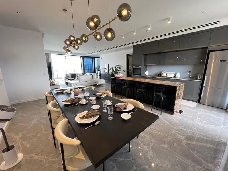 Dining features: large black dining table, white upholstered dining chairs, set of dinner plates, glassware, cutlery, decorative centerpiece, pendant lighting with multiple bulbs, marble flooring; style: modern; view: city. Kitchen features: grey cabinetry, stainless-steel appliances, built-in oven, microwave, stainless-steel fridge, kitchen island with bar seating, wooden countertop, sink, gooseneck faucet; style: modern; view: city. Living features: white leather sofa, coffee table, large windows, open layout, area rug; style: modern; view: city.