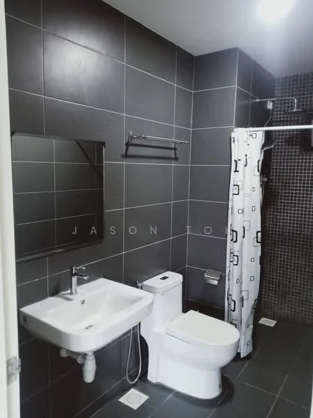 Bathroom features: grey tiled walls, black tiled flooring, single-sink vanity with wall-mounted faucet, one-piece toilet, shower area with glass partition, shower curtain with geometric pattern, framed mirror, towel rack, toilet paper holder, ceiling light; style: modern.