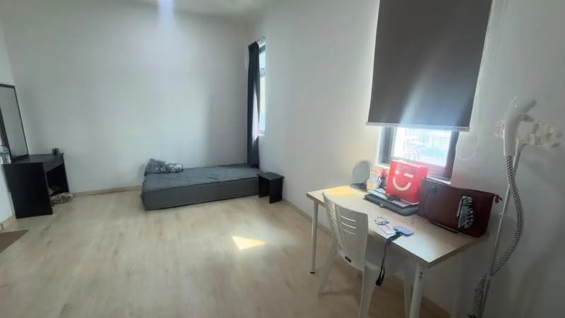 Bedroom features: light wood flooring, white painted walls, single bed with grey bedding, desk with chair, window with roller blinds, mirror, small black dresser, decorative pillow; style: minimalist.