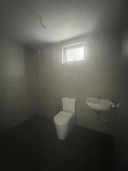 Bathroom features: white toilet, wall-mounted sink, small window, grey tiled walls, dark tiled flooring, ceiling light fixture, no visible storage, minimalist design; style: modern.