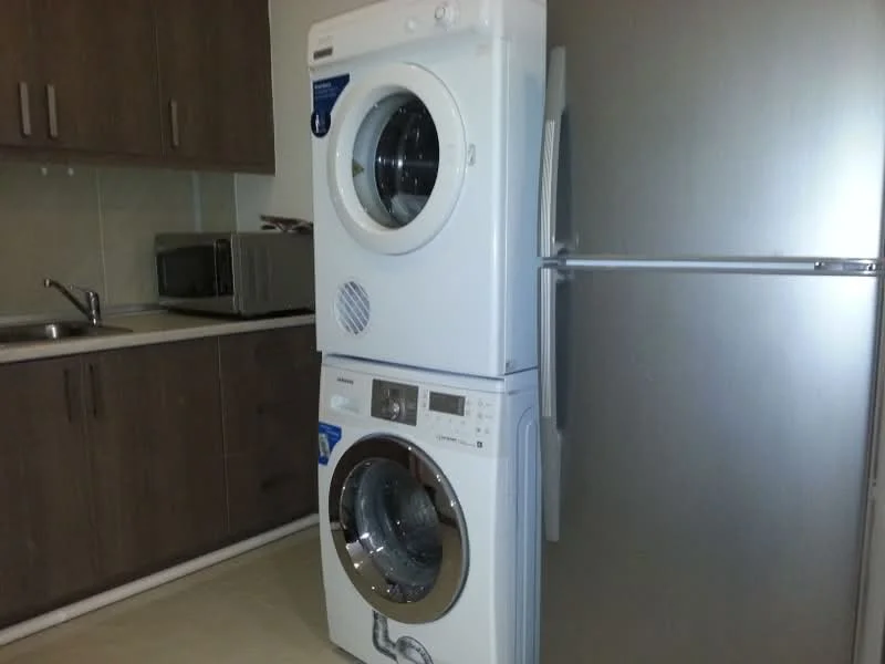 Laundry features: stacked washer and dryer, stainless-steel fridge, wood cabinetry, microwave, countertop, tile flooring, neutral wall color, single-bowl stainless-steel sink; style: modern.